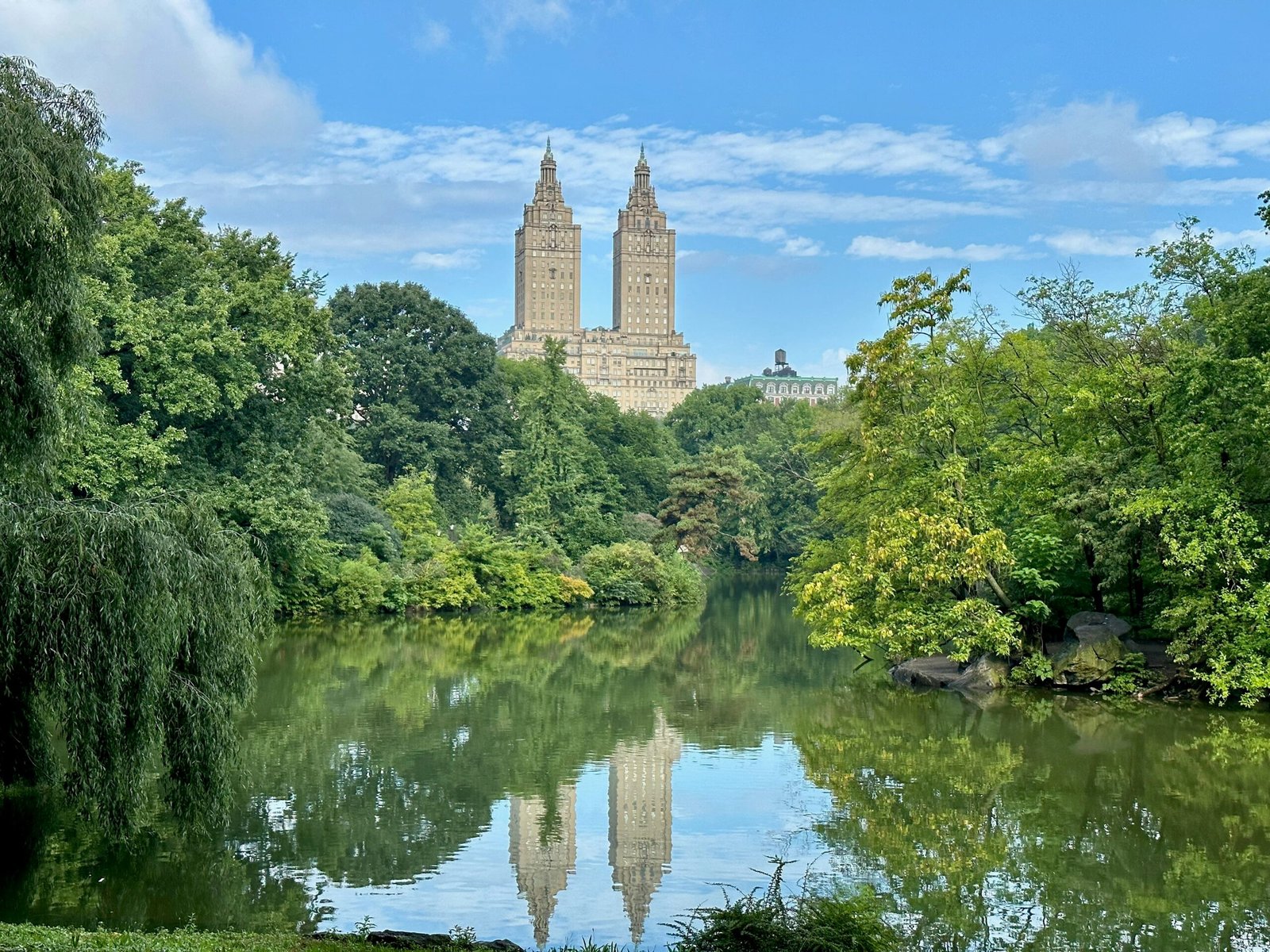 a lake surrounded by trees with a large building in the background